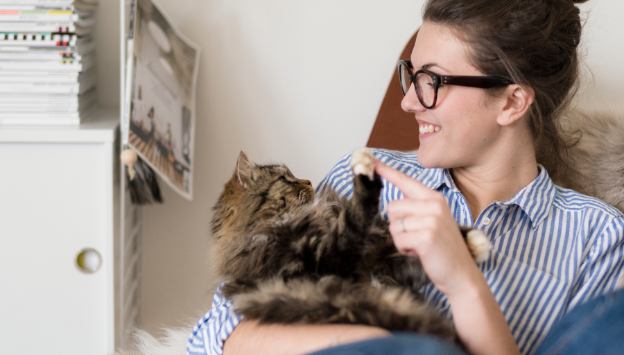 Eine Frau sitzt mit ihrer Katze auf dem Schoß und berührt deren Pfote mit ihrem Finger
