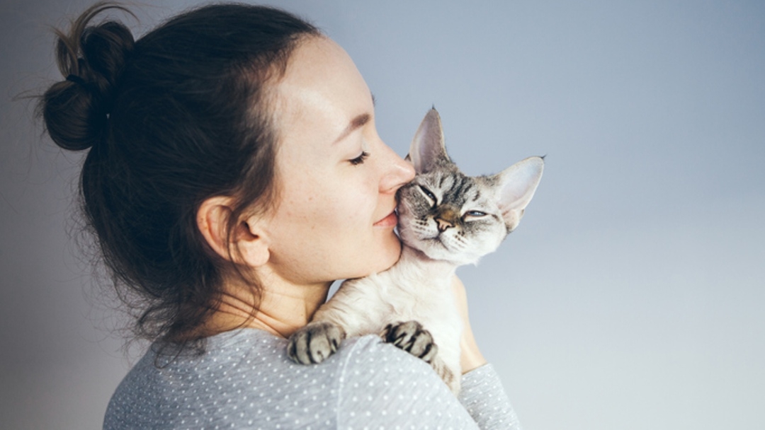 Frau küsst Katze auf Schulter