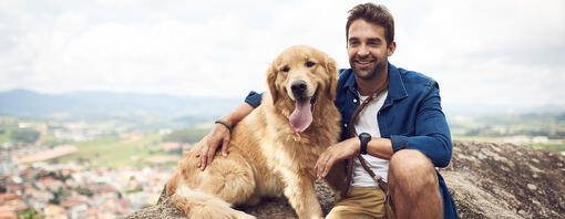 Hund sitzt mit Mann auf dem Berg